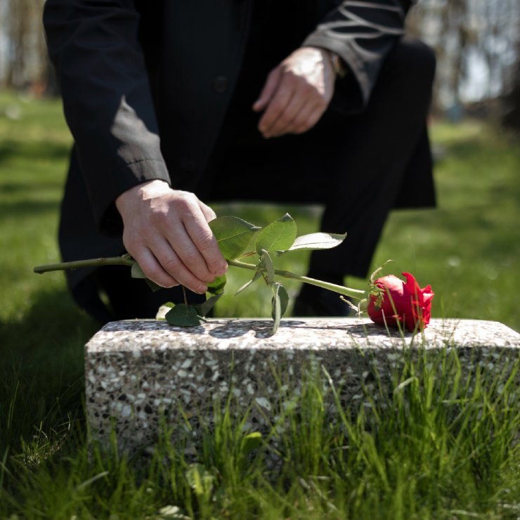 Man bringing a rose to a tombstone at the cemetery